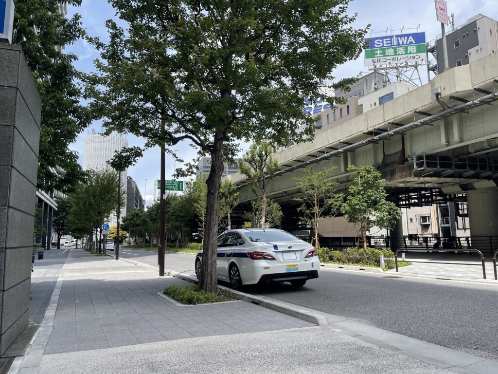 都内挨拶回りの貸切送迎|ビル外待機からエントランスへ即時アプローチ 都内の企業挨拶回りでビル外に待機する藤﨑タクシーのクラウン。お客様が出られたらすぐにエントランスへ車付けできるようスタンバイ