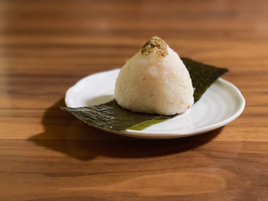 おにぎりアクションに自分で参加して作ったカニ味噌おにぎり。のりを敷いた白い皿に盛りつけ、木のテーブルの上で撮影。