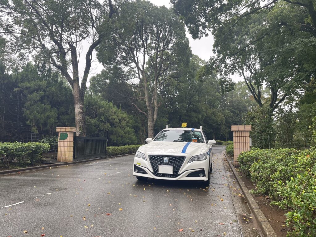 千葉県の立野クラシックゴルフ倶楽部正門前に停車するFUJISAKI TAXIのクラウン個人タクシー。雨上がりの並木道に映える白のクラウン。
