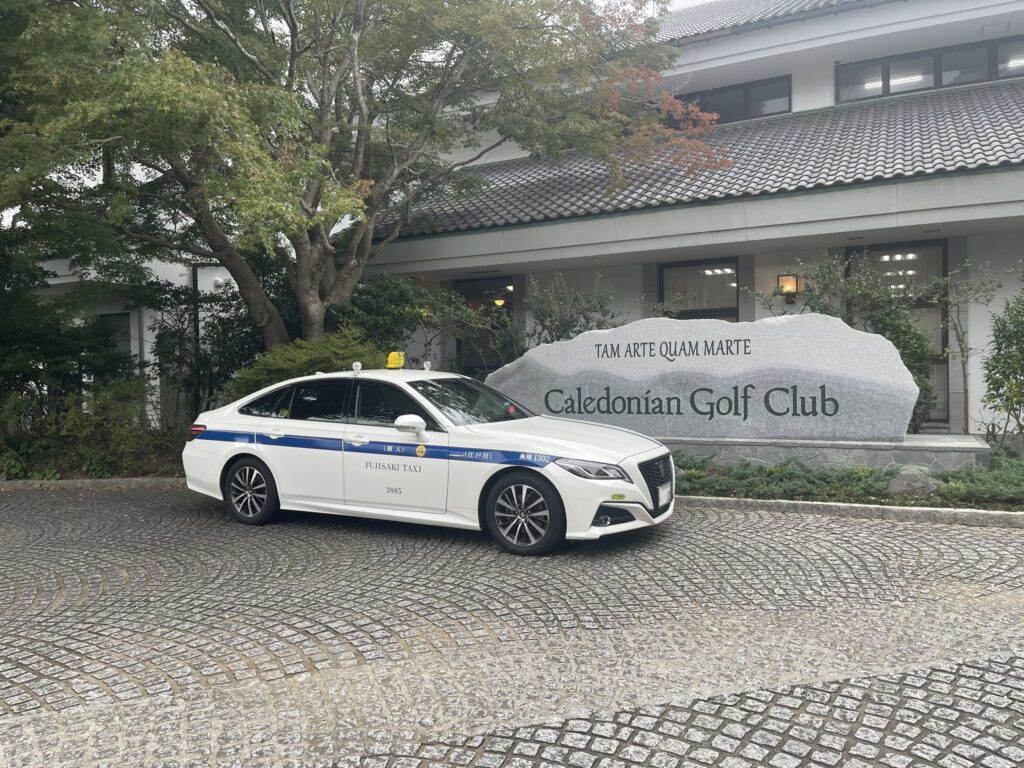 カレドニアン・ゴルフクラブのクラブハウス前で待機する藤崎タクシーのクラウンセダン。石碑の前で静かに着車準備を整える様子。