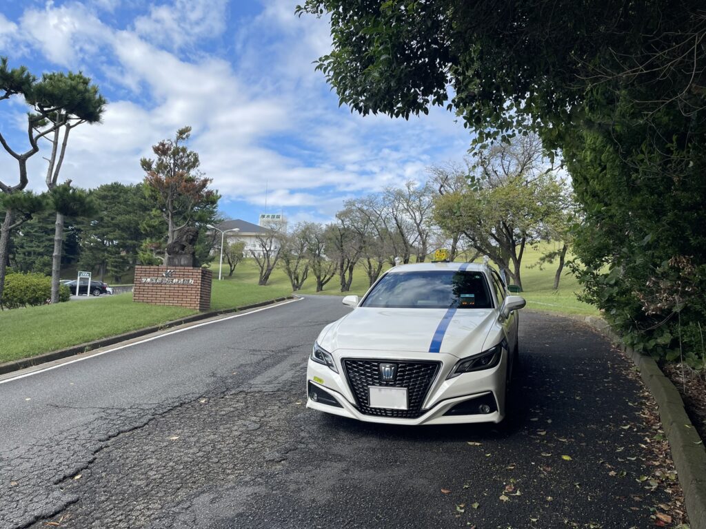 厚木国際カントリー倶楽部のエントランス前に到着した藤崎タクシーのクラウン。晴天の下、ゴルフ場の門標とクラブハウスが見える。
