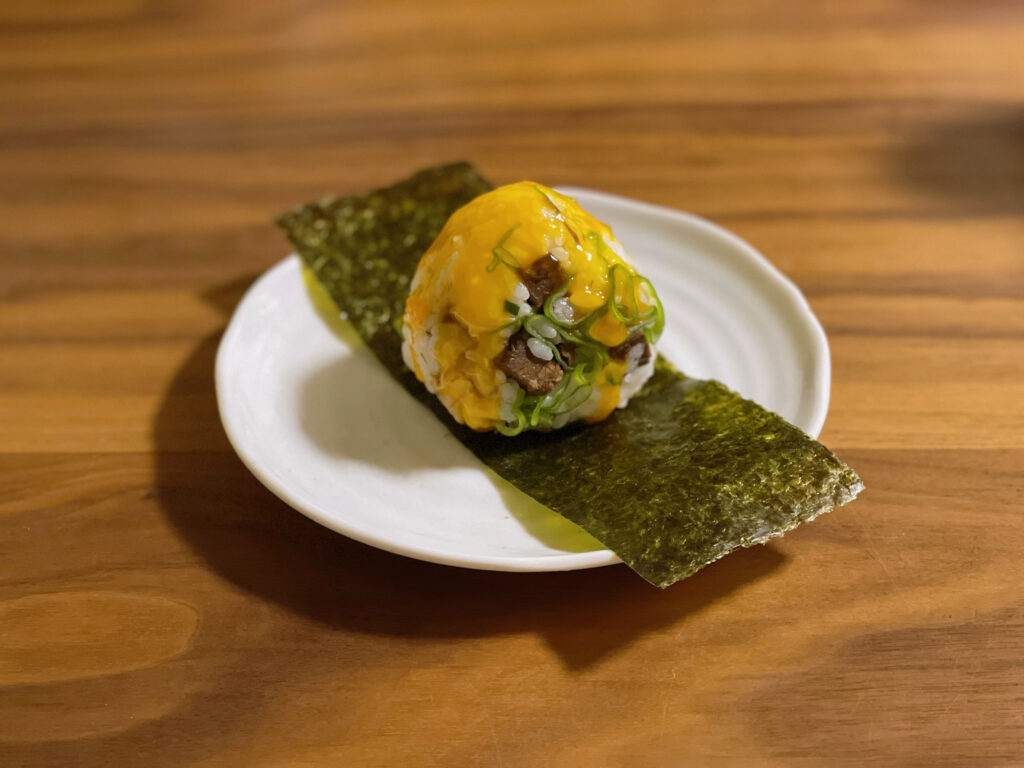 おにぎりアクション用に撮影した、玉子かけ焼豚おにぎり。焼豚入りのご飯に卵黄ソースと刻みねぎをのせ、海苔の上に盛り付けた一品。