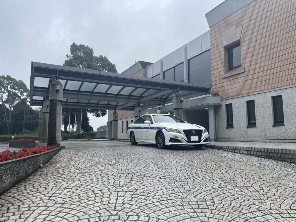 立野クラシックゴルフ倶楽部のエントランス前に停車する藤崎タクシーのクラウン。雨上がりの石畳と落ち着いた雰囲気のクラブハウス。