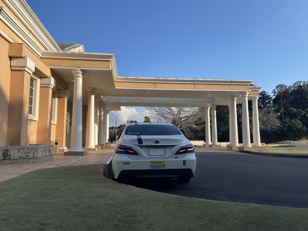 太平洋クラブ成田コースのクラブハウス前で、キャディーバッグ積み込み完了後に帰路待機する藤﨑タクシーのクラウン